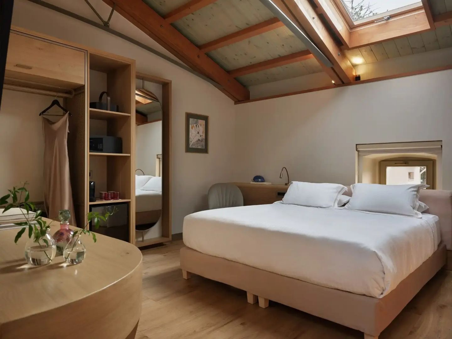 Helles Hotelzimmer mit Doppelbett, Holzdach mit Dachfenster und offenem Kleiderschrank.