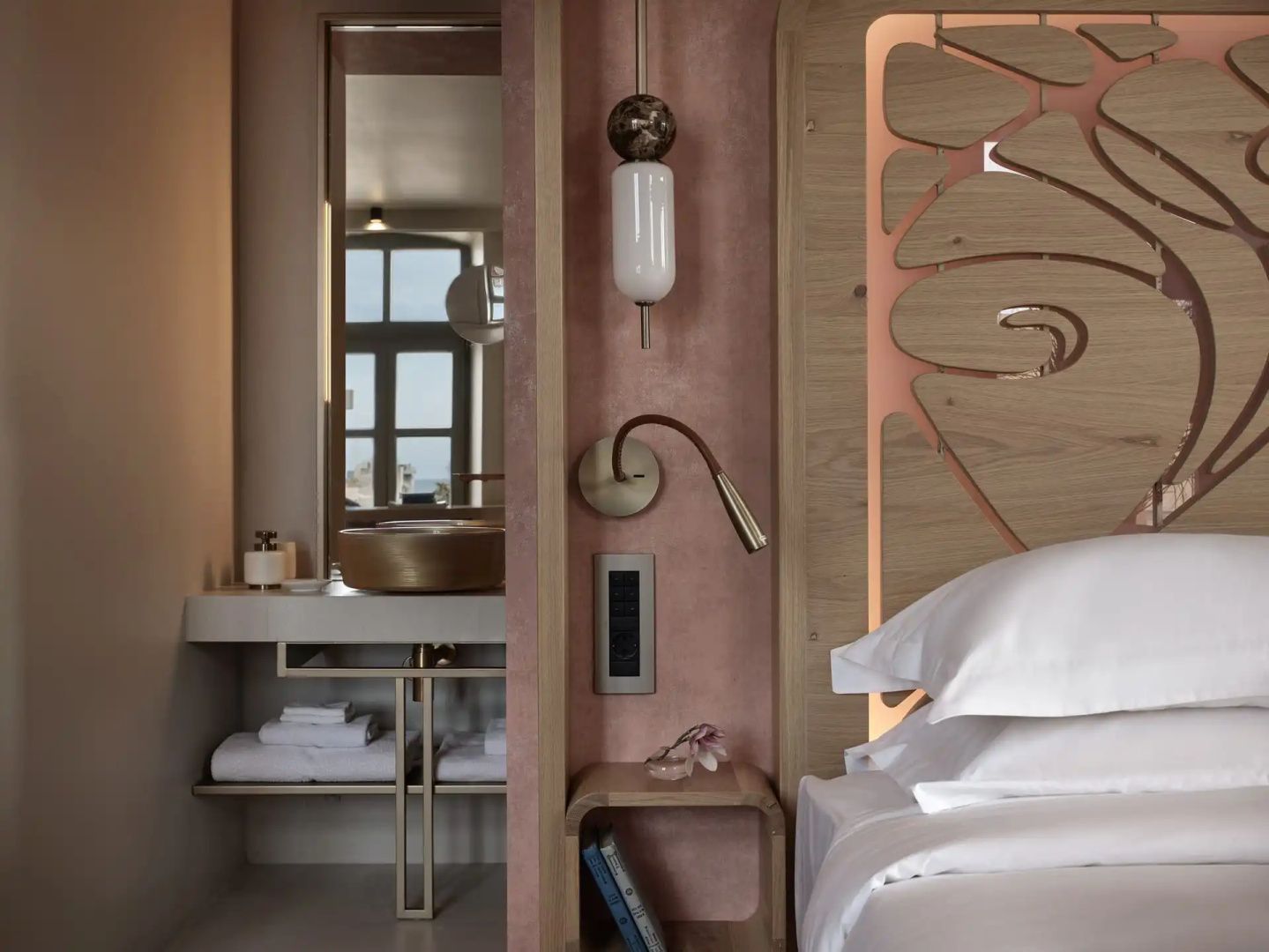 Ausschnitt eines Hotelzimmers mit Nachttisch, Wandlampe und Waschbereich.