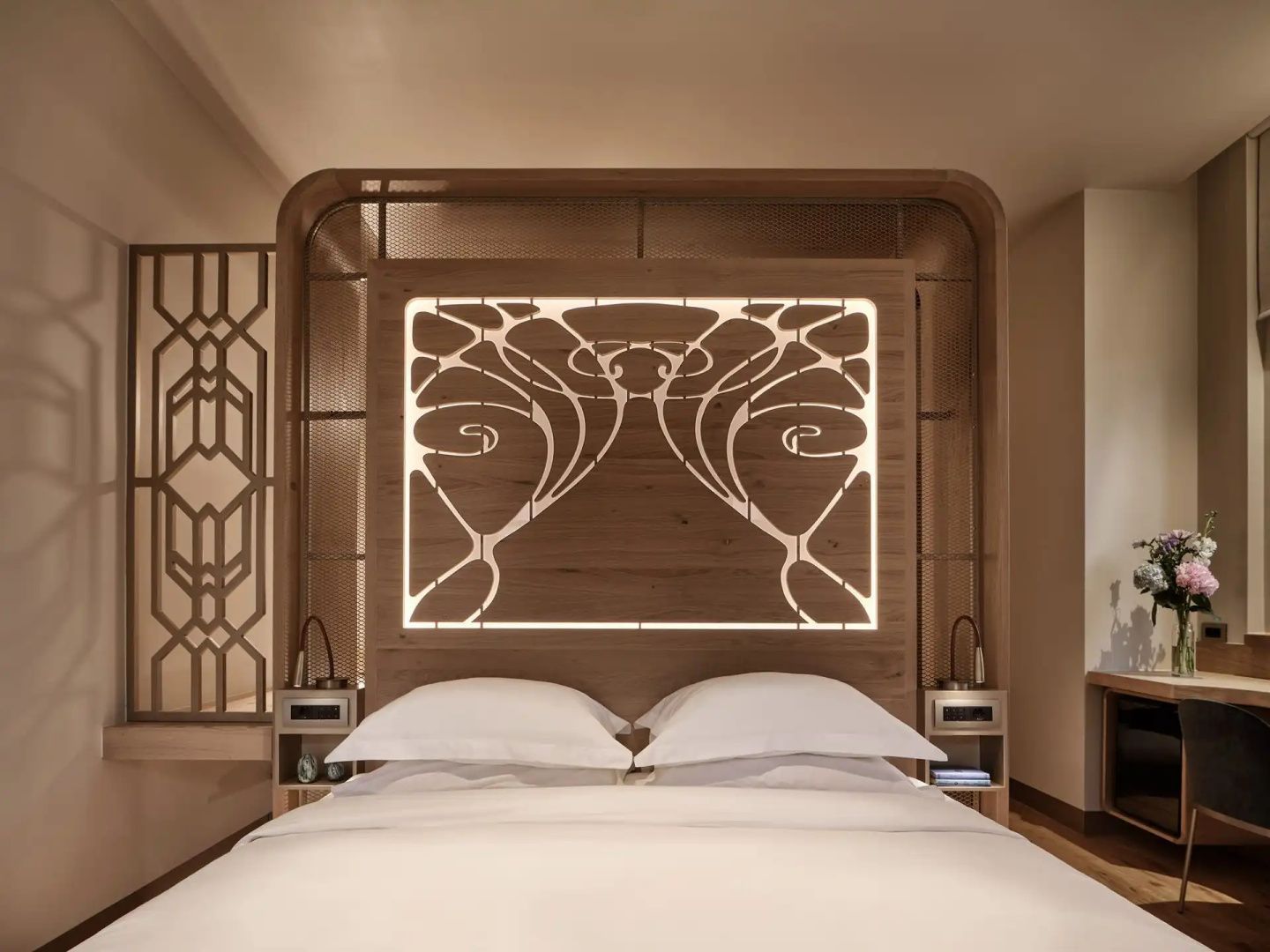 Bett in einem Hotelzimmer mit beleuchtetem Holzkopfteil, zwei Kissen und Wandverkleidung.