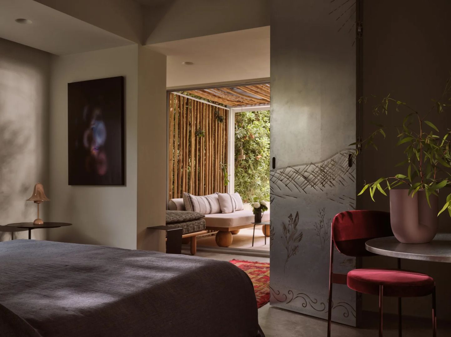 Modernes Hotelzimmer mit Schiebetür aus Metall, rotem Stuhl und Blick auf eine überdachte Terrasse.