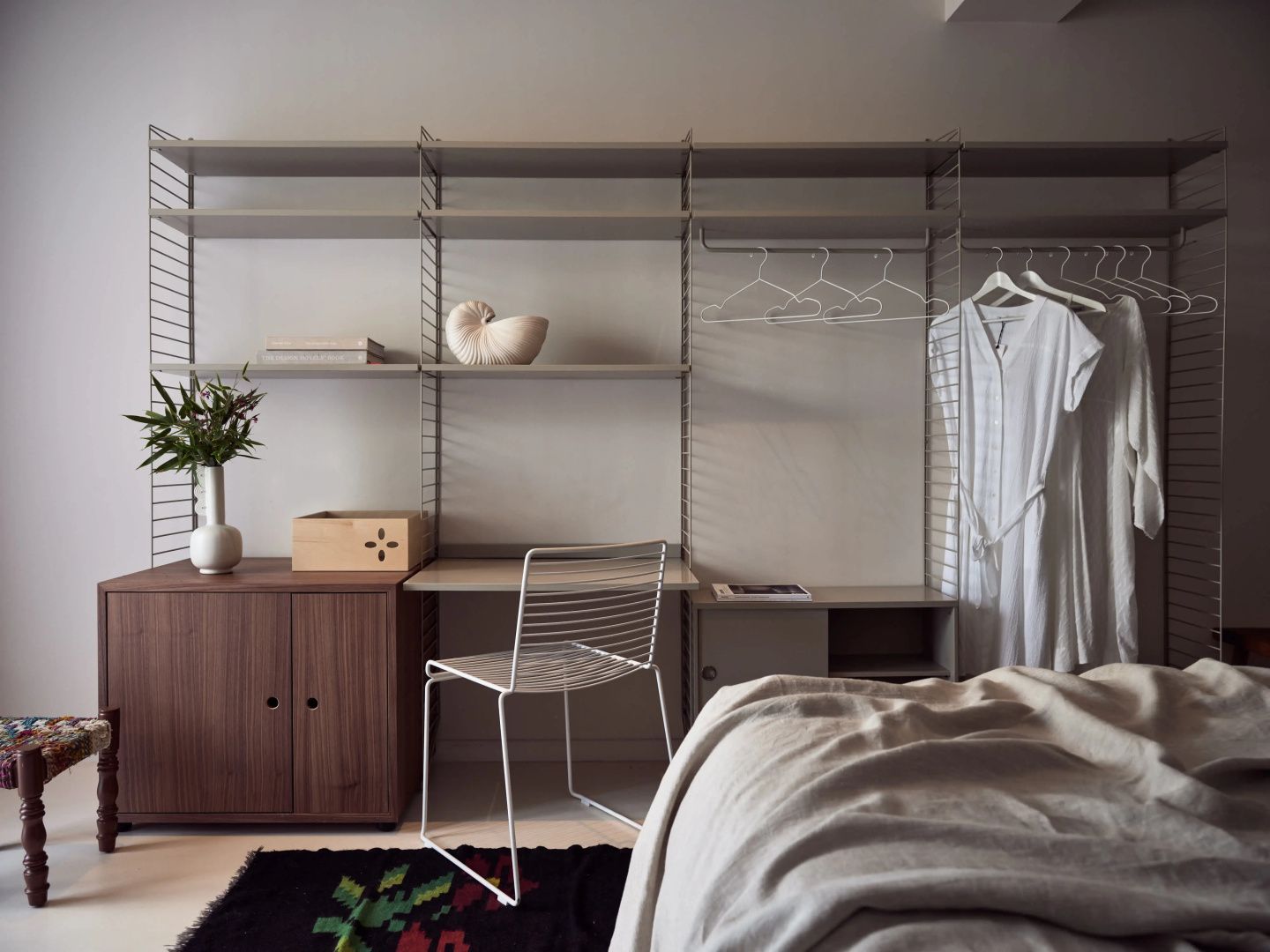 Modernes Zimmer mit Regalsystem, Schreibtisch aus Metall und Holz sowie Bettbereich.