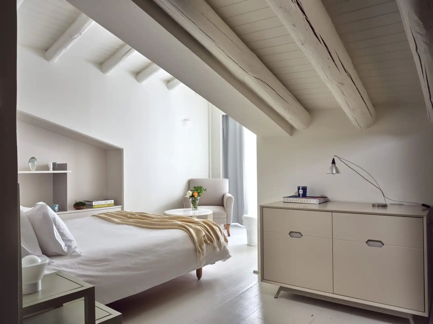 Helles Zimmer unter einer Holzbalkendecke mit Doppelbett und Sessel.