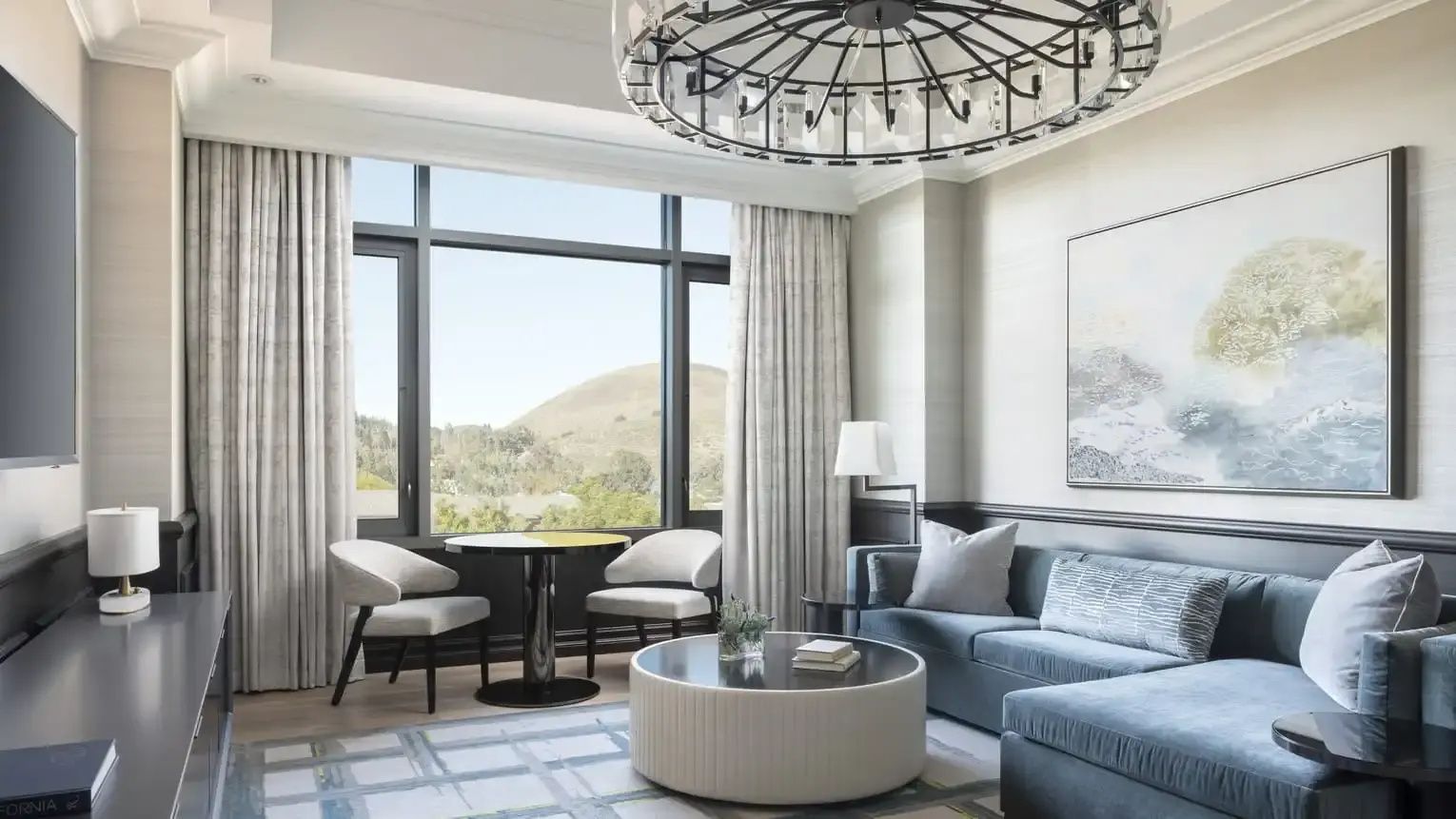 Sitzbereich einer Suite mit blauem Sofa, rundem Couchtisch und Fenster mit Blick ins Grüne.