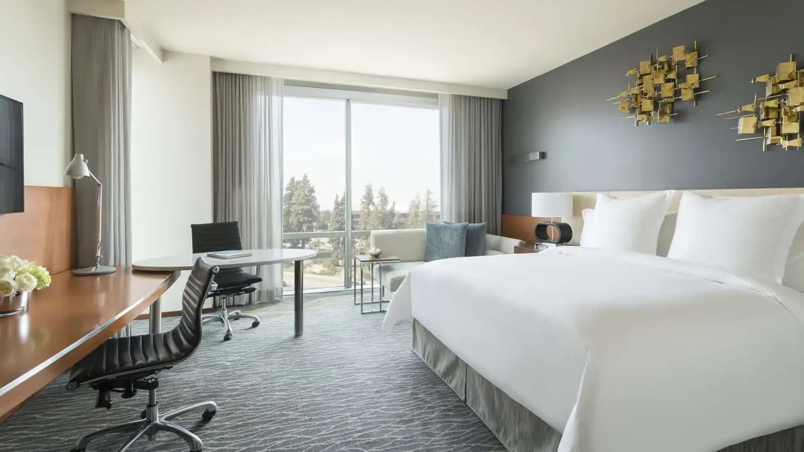 Hotelzimmer mit Kingsize-Bett, Schreibtisch und Sofa vor der Fensterfront.
