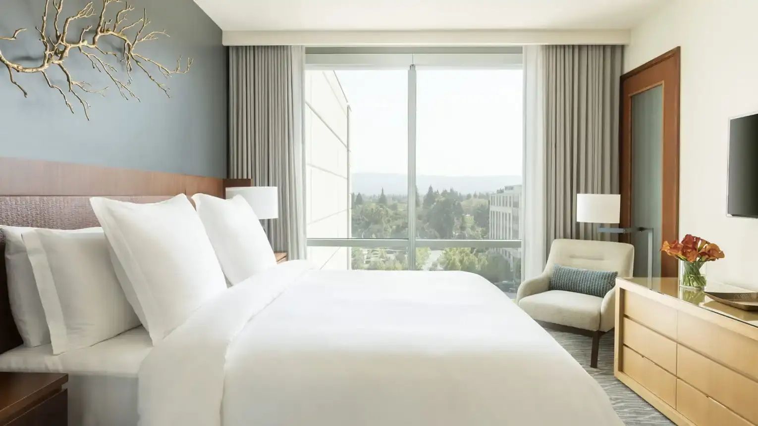 Doppelbett mit weißen Kissen an einer Wand neben einem großen Fenster mit Ausblick.