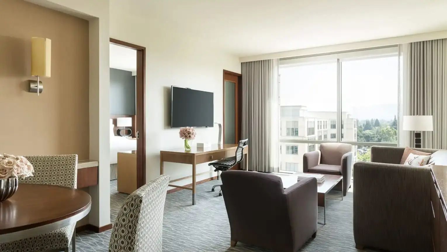 Wohnbereich einer Suite mit Schreibtisch, Fernseher, Sesseln und großem Fenster.