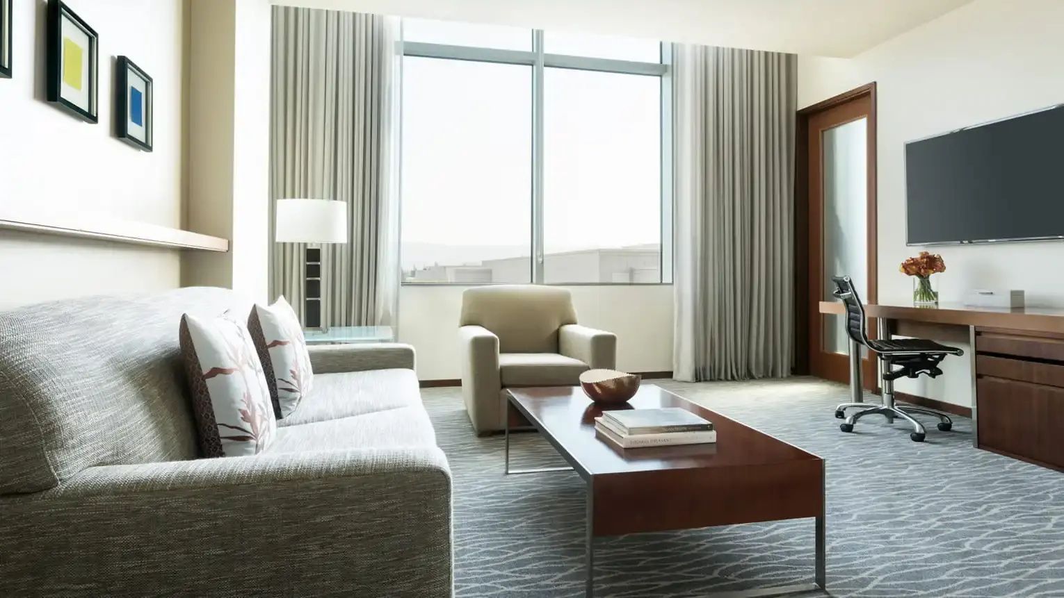 Wohnbereich einer Suite mit grauem Sofa, Holzcouchtisch, Sessel und großer Fensterfront.