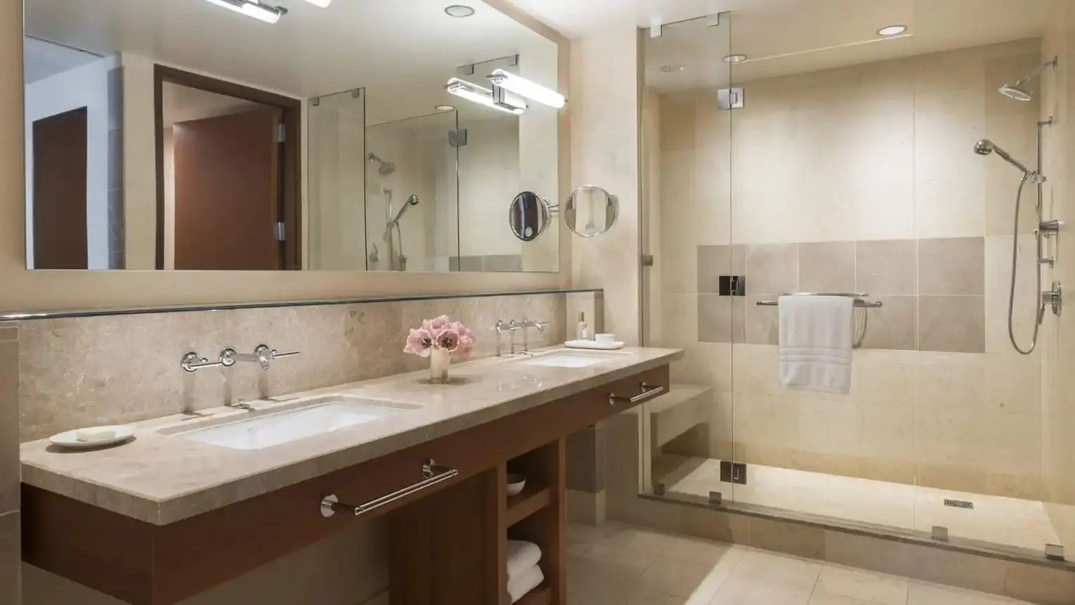 Badezimmer mit Doppelwaschtisch, großem Spiegel und einer verglasten Dusche.