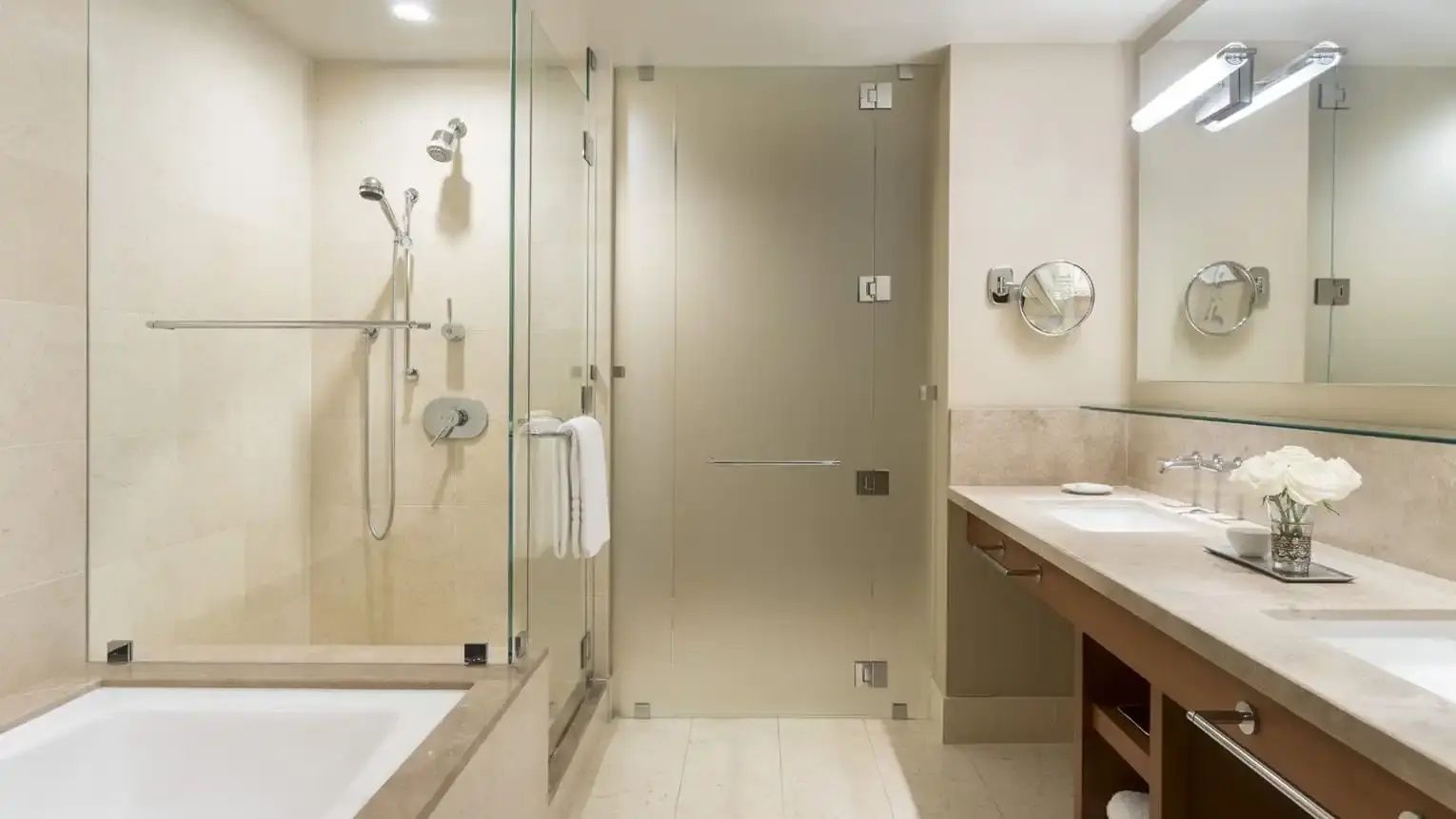 Badezimmer mit verglaster Dusche, Badewannenrand und einem Waschtisch mit Spiegel.