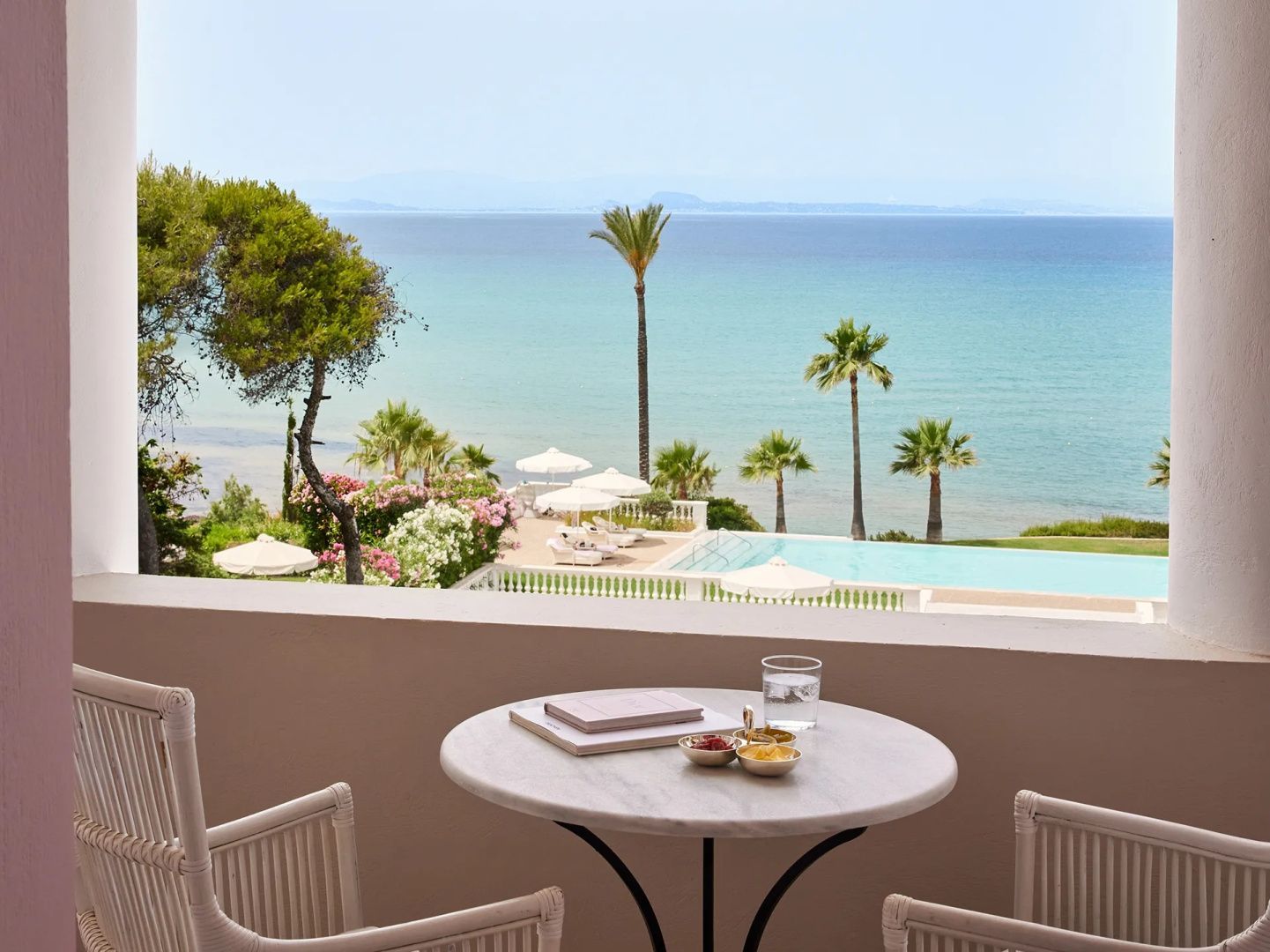 Blick von der Terrasse mit Tisch und Stühlen auf den Swimmingpool und das Meer.
