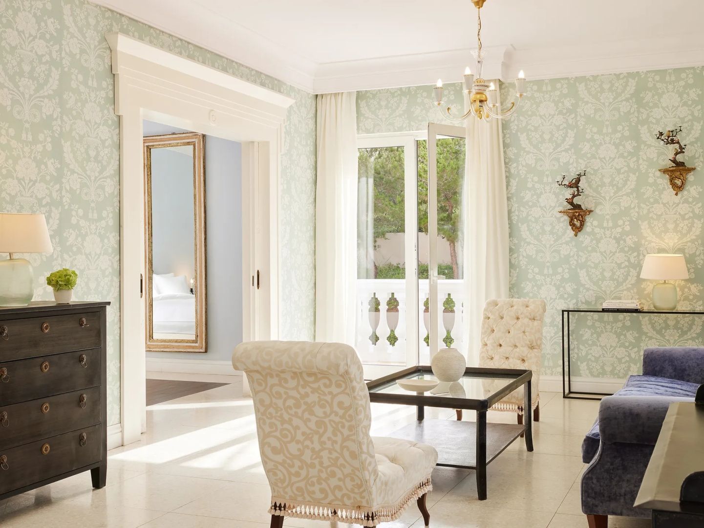 Wohnzimmer einer Suite mit hellgrüner Tapete, zwei Sesseln und einer Glastür zum Balkon.