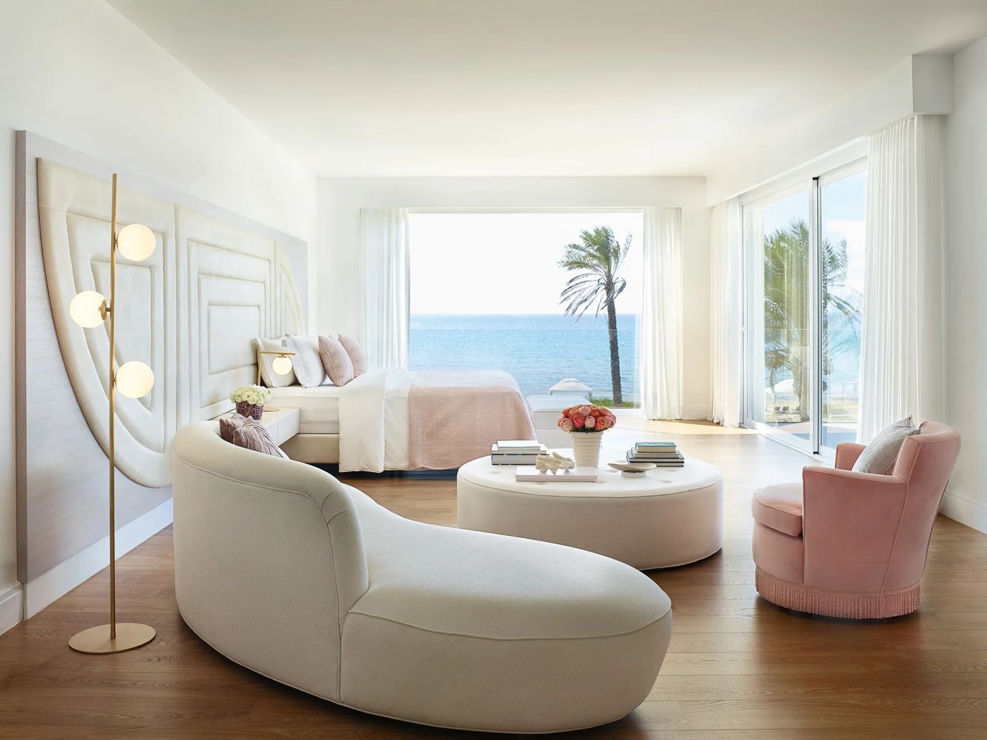 Großzügiges Schlafzimmer mit cremefarbener Liege, Couchtisch und Panoramablick auf Meer und Palme.