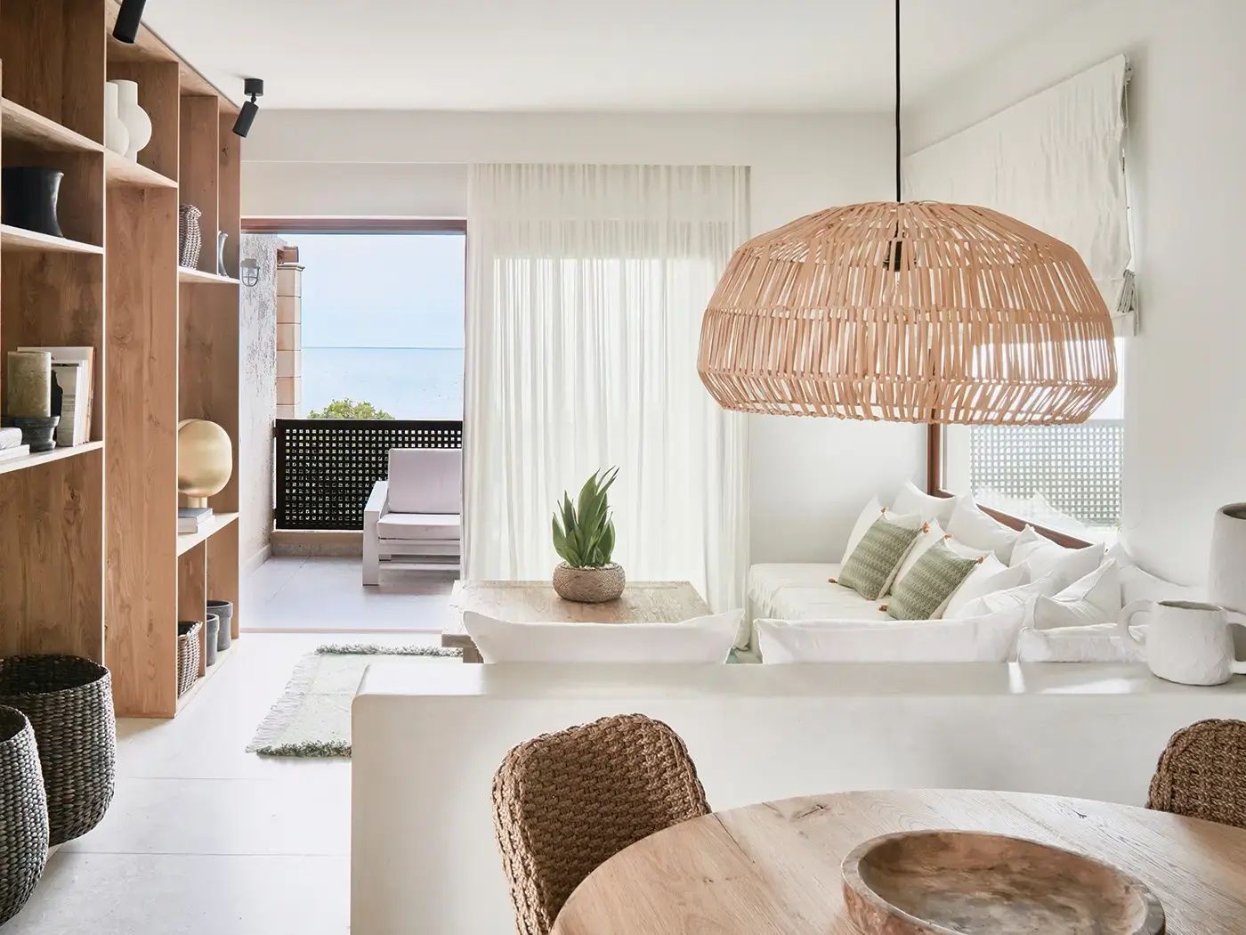 Helles Wohnzimmer mit weißem Sofa, großem Rattanlampenschirm und Blick auf den Balkon mit Meerblick.