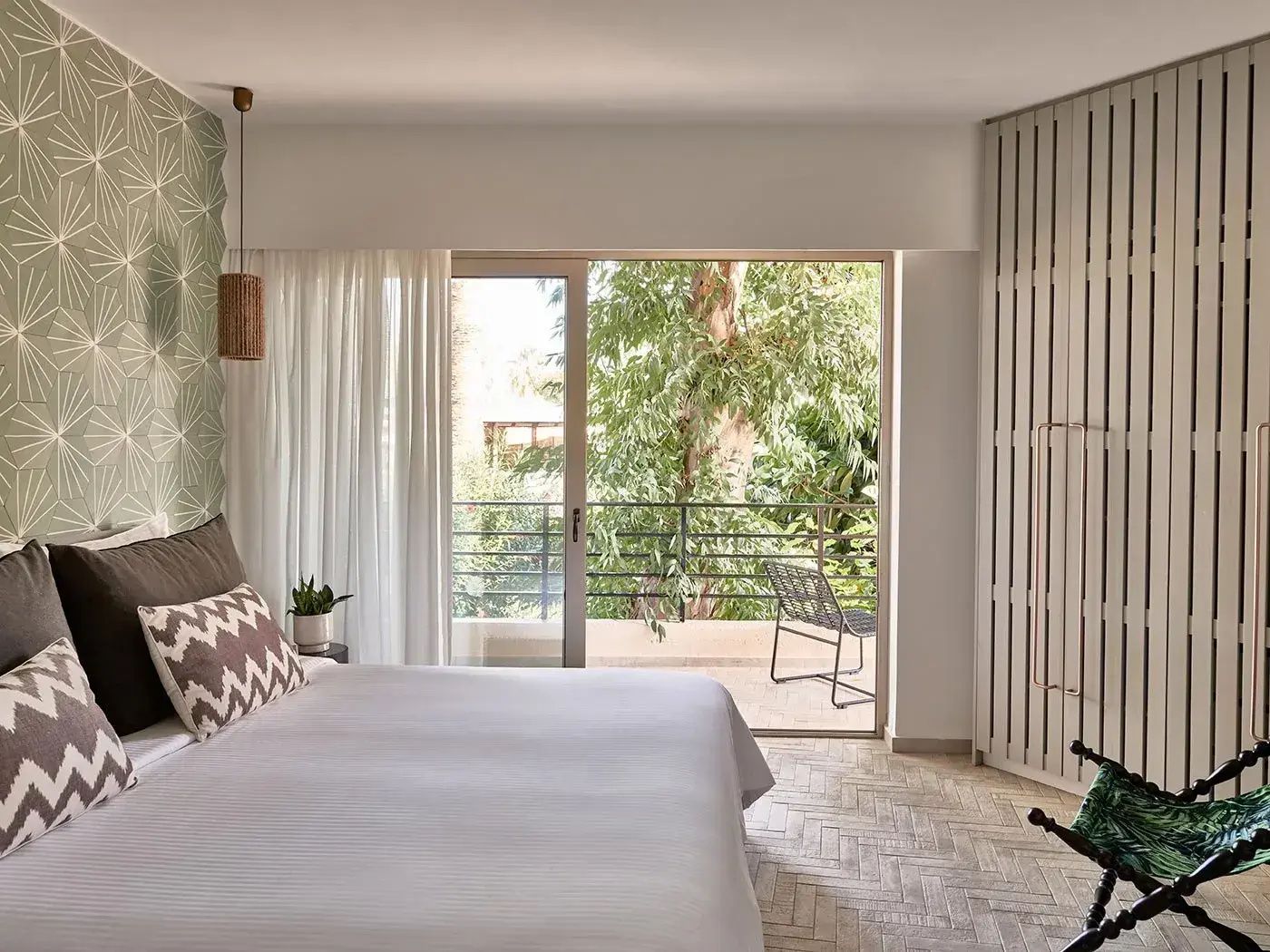 Helles Schlafzimmer mit Doppelbett, Vorhängen und Balkontür mit Blick ins Grüne.