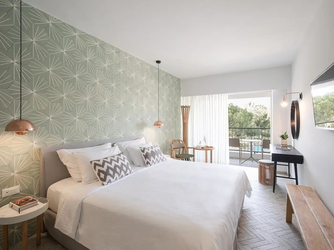 Helles Hotelzimmer mit großem Doppelbett, grüner Motivwand und Balkonzugang.