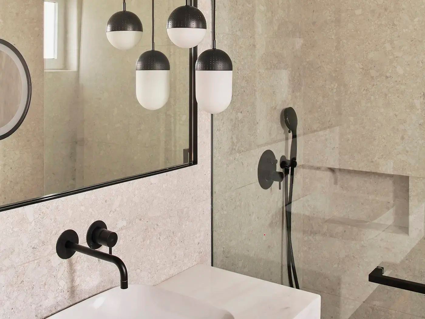 Badezimmer mit weißem Waschbecken, schwarzer Armatur und verglastem Duschbereich.
