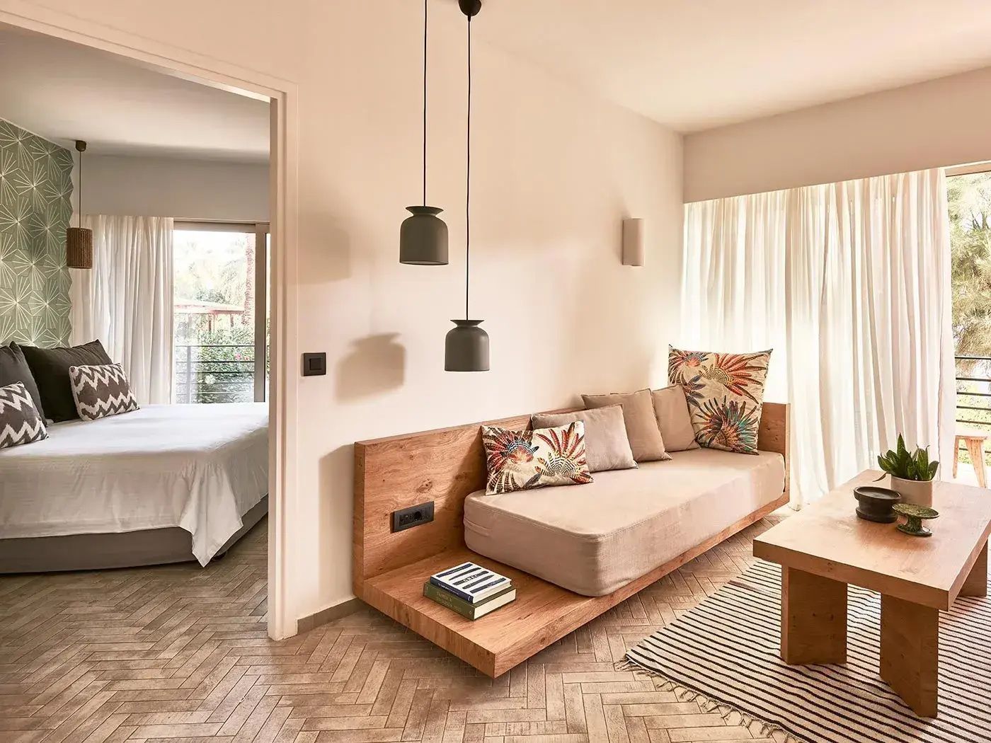 Wohnbereich einer Suite mit Holzsofa, Kissen und Durchgang zum Schlafzimmer.