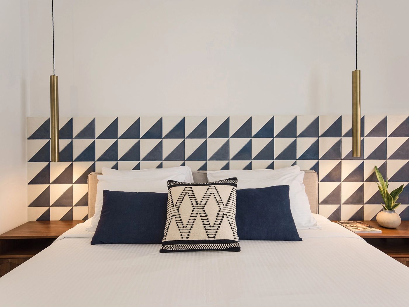 Doppelbett mit weißen Kissen, blauen Dekokissen und geometrisch gefliester Kopfwand