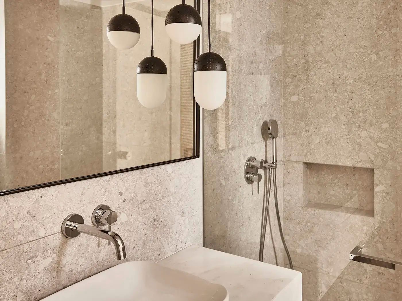 Waschbecken mit Armatur aus Chrom, Hängelampen und hellen Wandfliesen im Badezimmer.