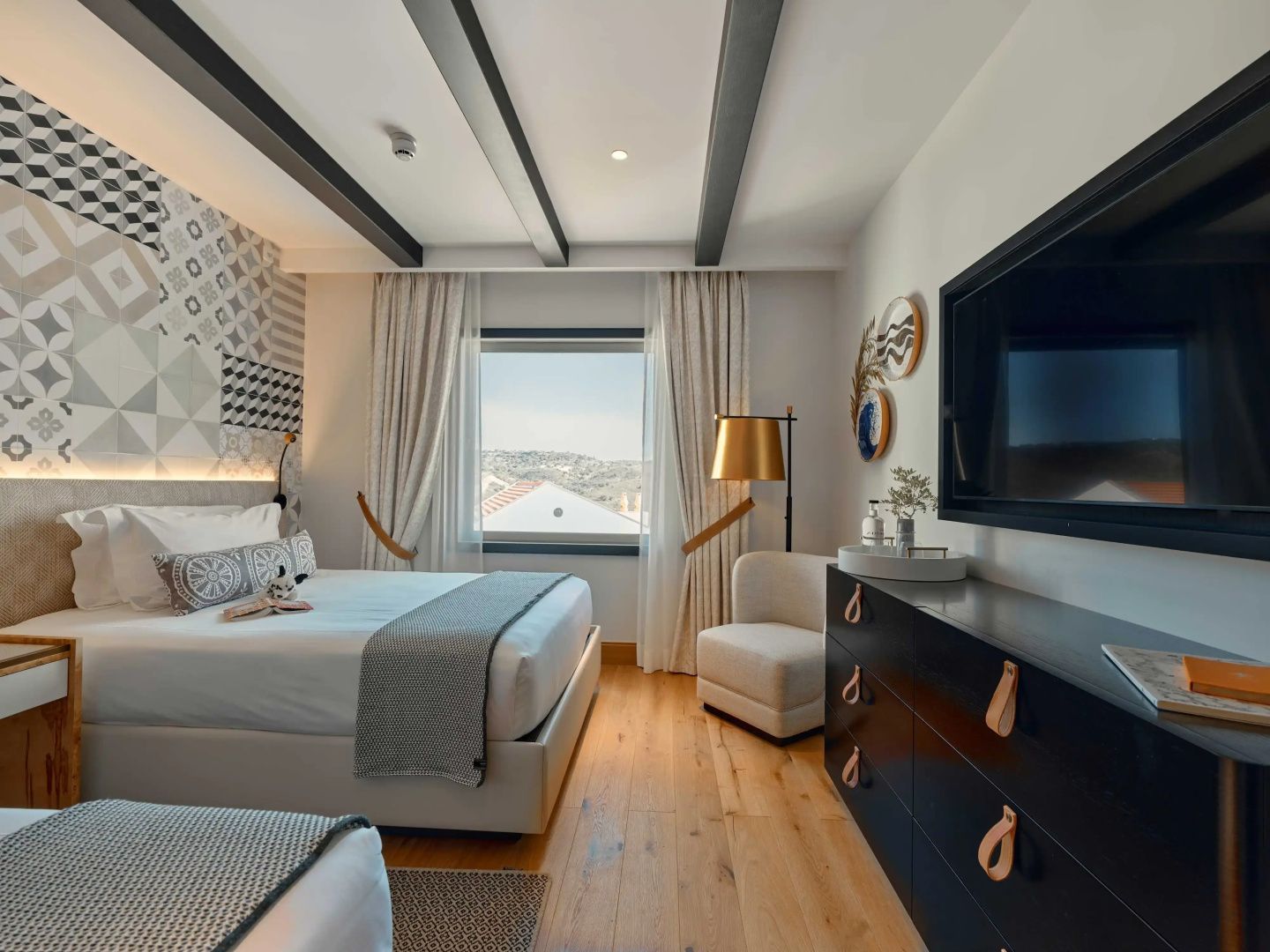 Hell eingerichtetes Schlafzimmer mit Bett, Fenster zum Außenbereich und Fernseher.