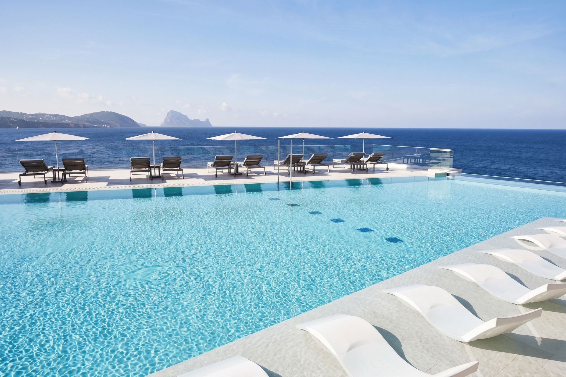 Infinity-Pool im 7Pines Resort Ibiza mit Sonnenliegen und traumhaftem Blick auf das Mittelmeer und die Insel Es Vedrà.