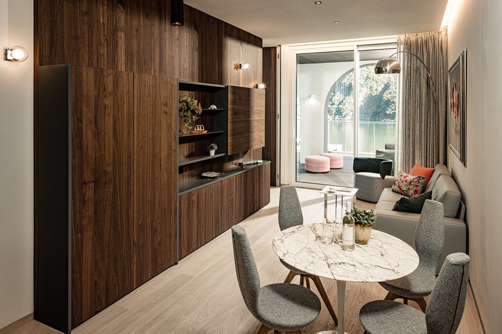 Wohnbereich mit rundem Esstisch, Holzschränken und Zugang zur Terrasse mit Seeblick.