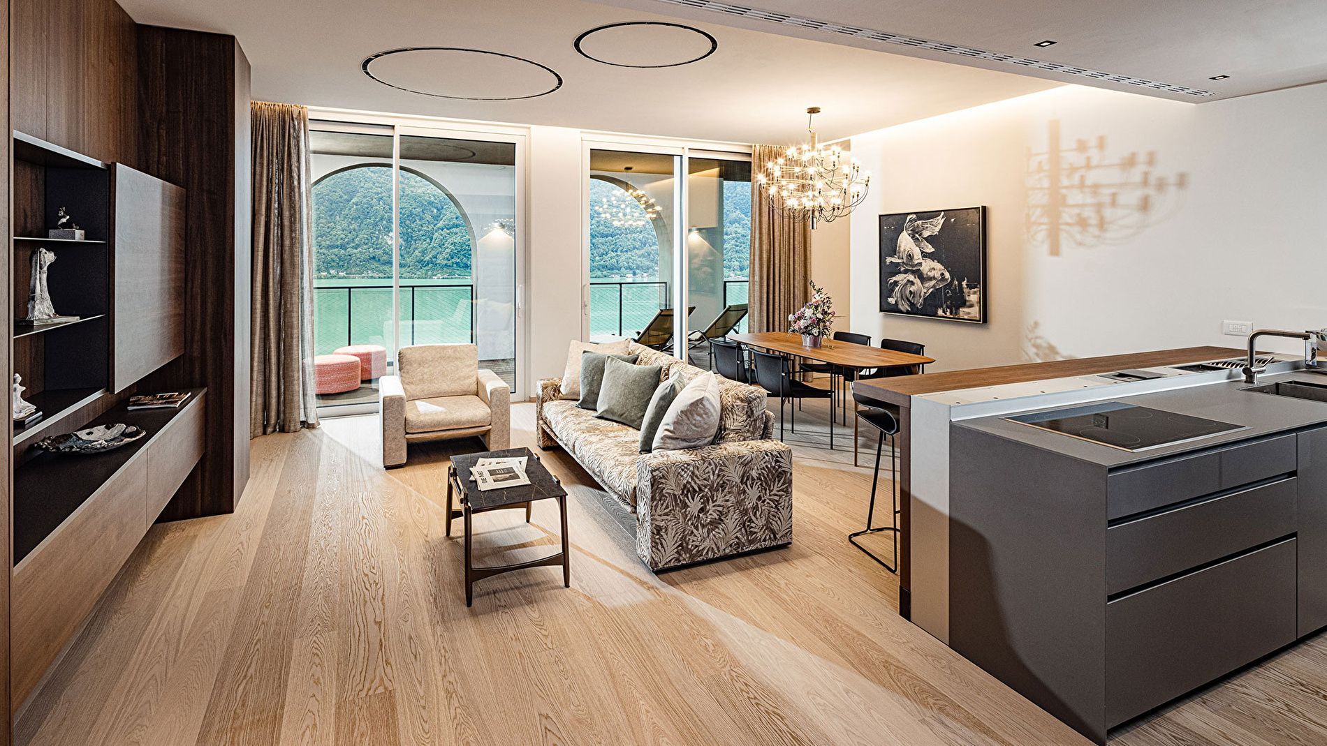 Moderner Wohnbereich mit Sofa, Esstisch und großen Glasfronten zum Balkon mit Seeblick.