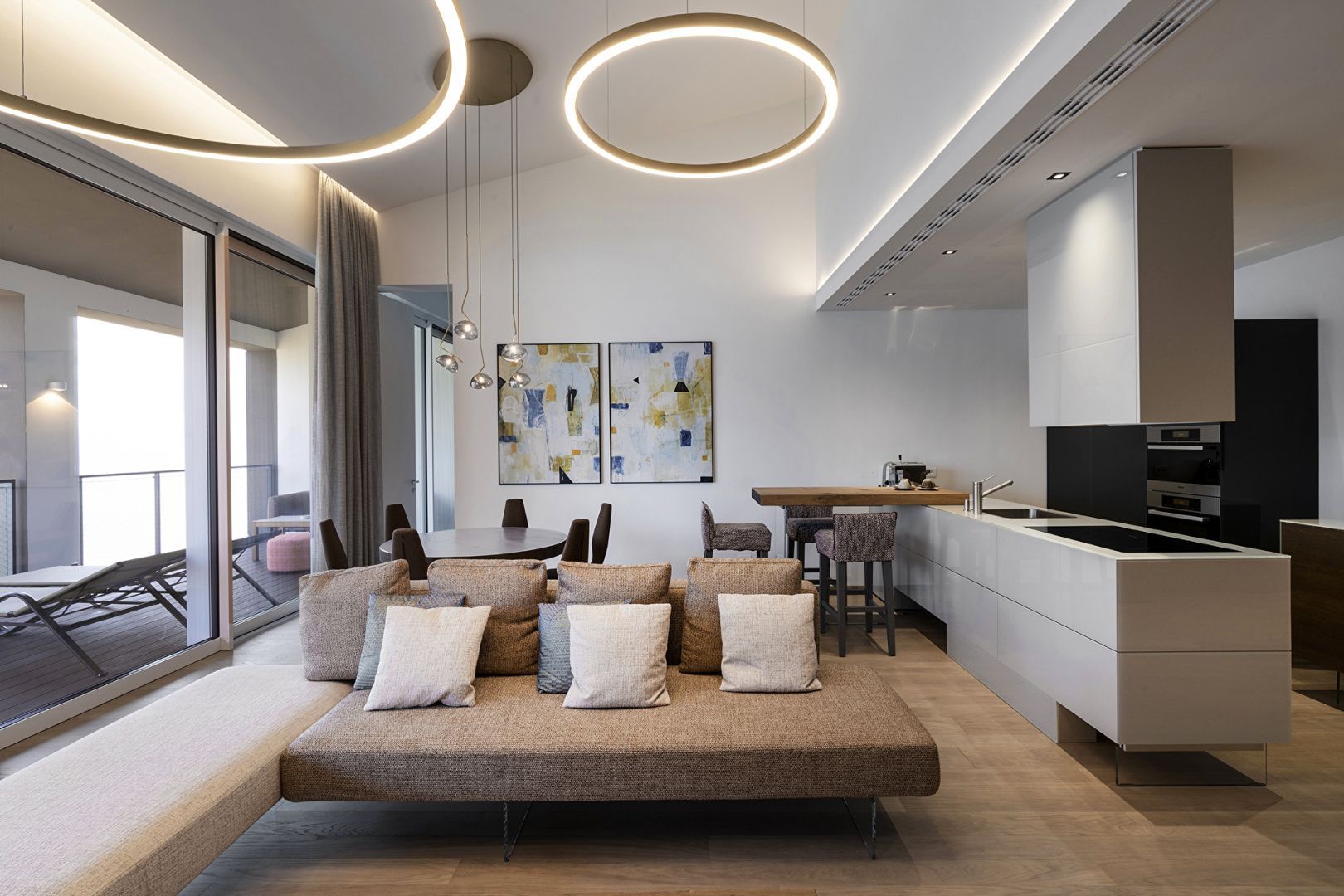 Wohnbereich mit beigem Sofa, modernen Ringleuchten und integrierter Küche.