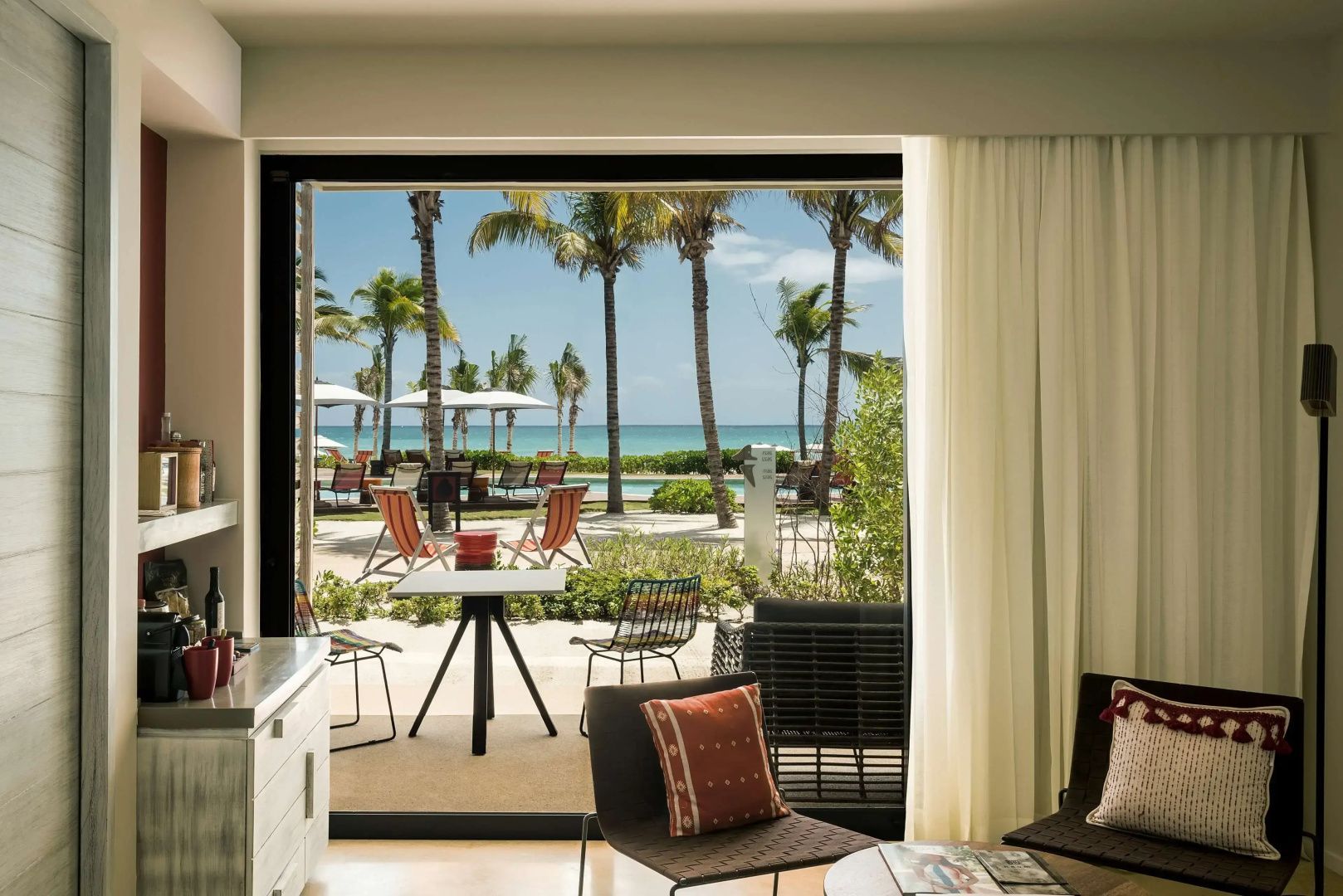 Blick von einer Terrasse auf Palmen, den Swimmingpool und das dahinterliegende Meer.