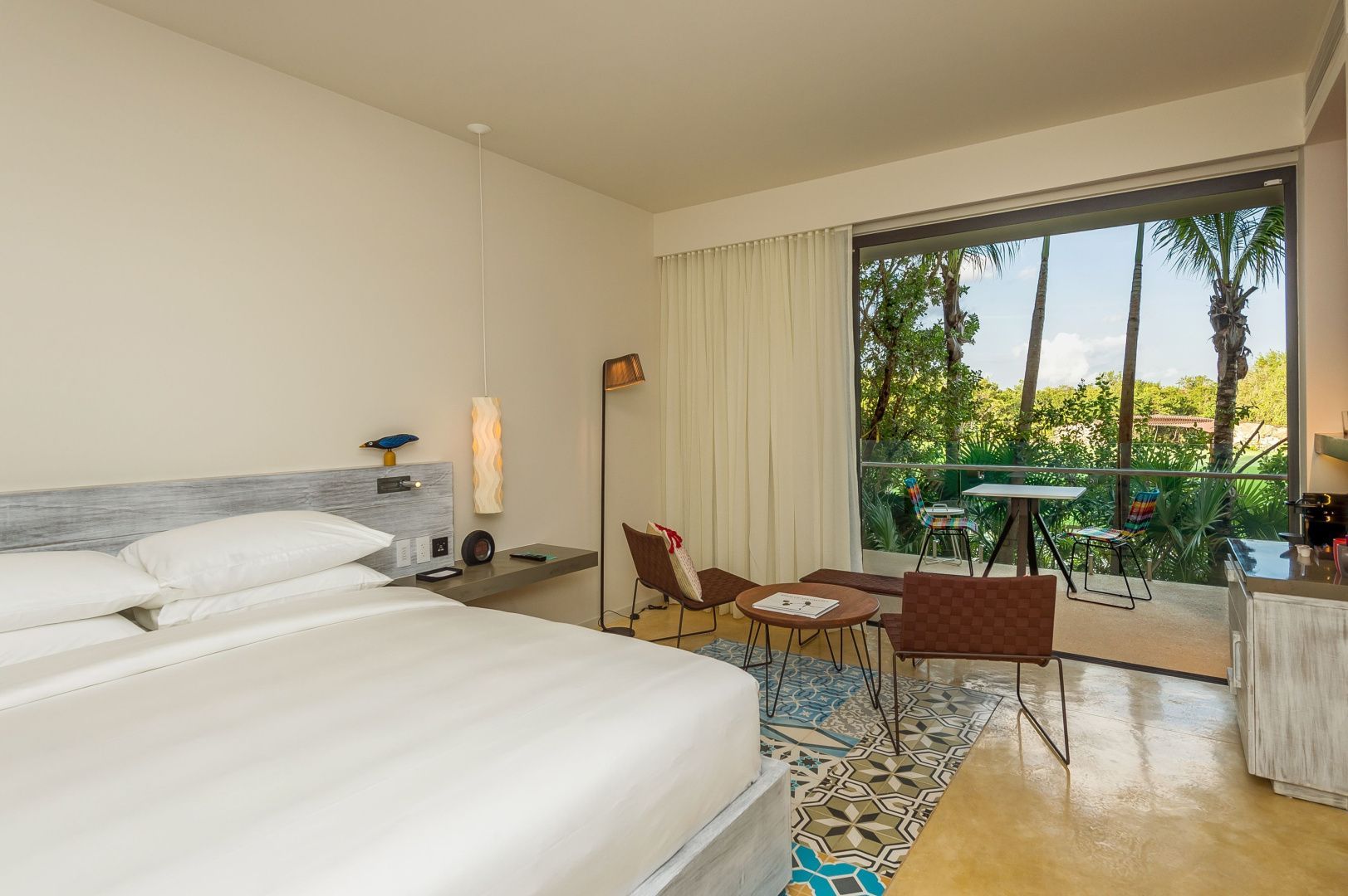 Modernes Schlafzimmer mit weißem Bett, Sitzbereich und Blick ins Grüne.