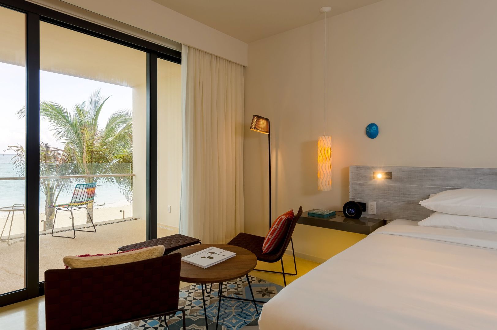 Hell eingerichtetes Hotelzimmer mit Doppelbett, Sitzbereich und Balkon mit Palmenblick.