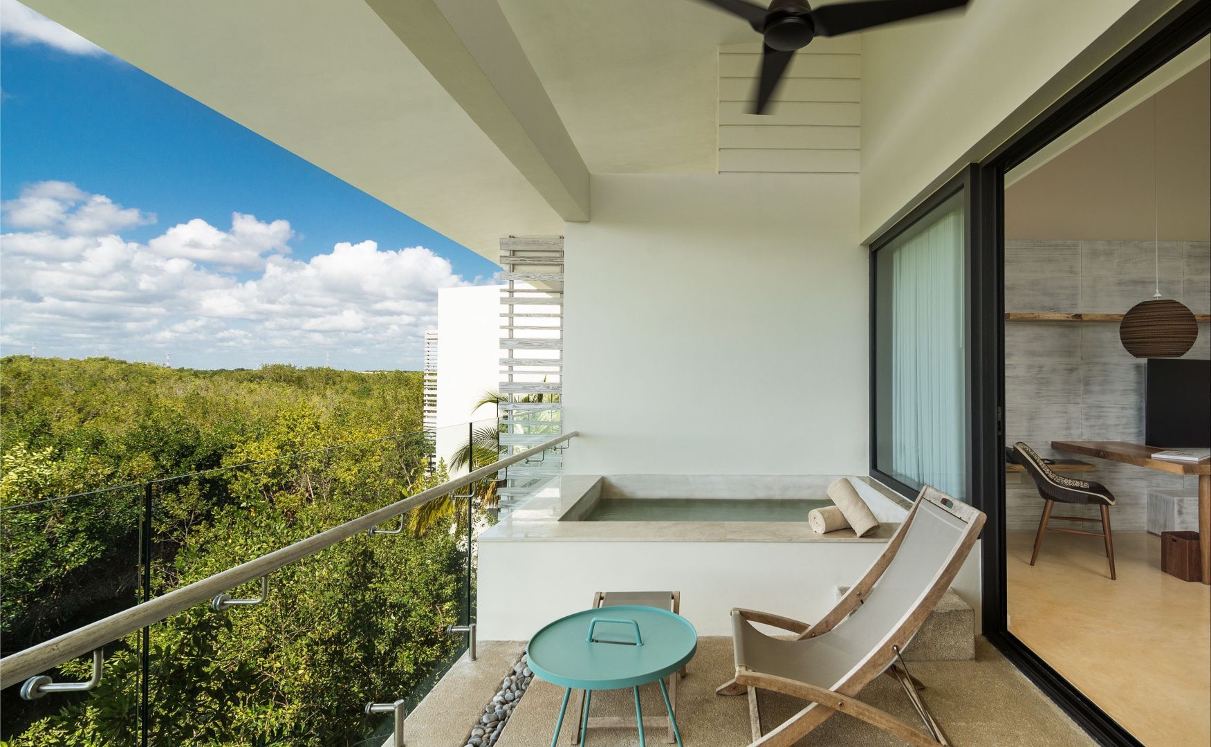 Überdachter Balkon mit kleinem Pool, Liegestuhl und Weitblick über dichte grüne Bäume unter blauem Himmel.