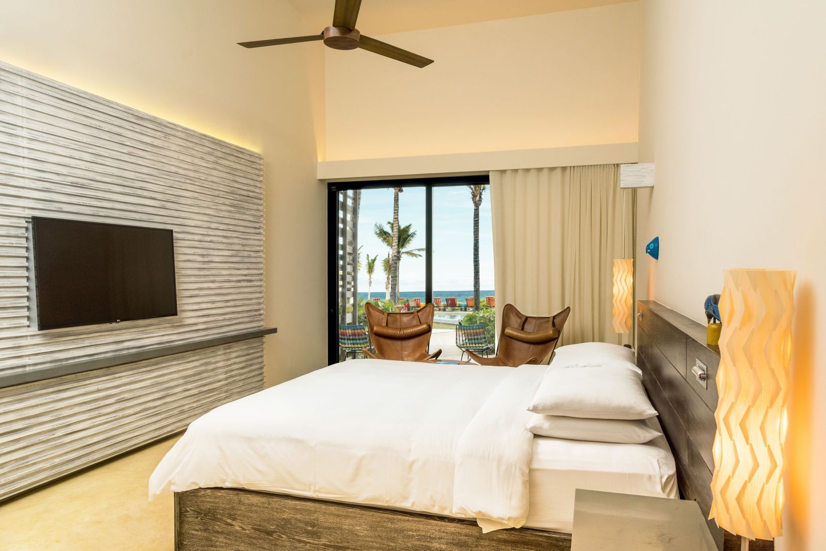 Hell eingerichtetes Hotelzimmer mit Doppelbett, Flachbildfernseher und Blick ins Freie.