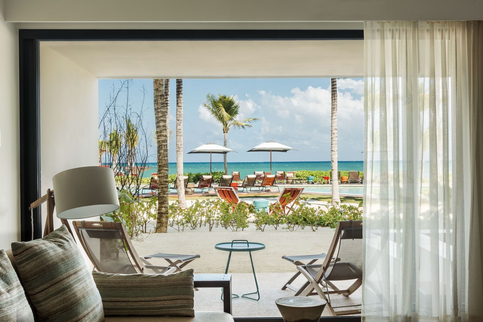 Terrasse mit zwei Liegestühlen und freiem Blick über Grünflächen und Palmen auf den Strand und Ozean.