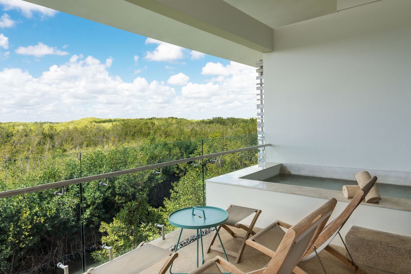 Sonniger Hotelbalkon mit Sitzgelegenheiten und Panoramablick auf ein dichtes grünes Waldgebiet.