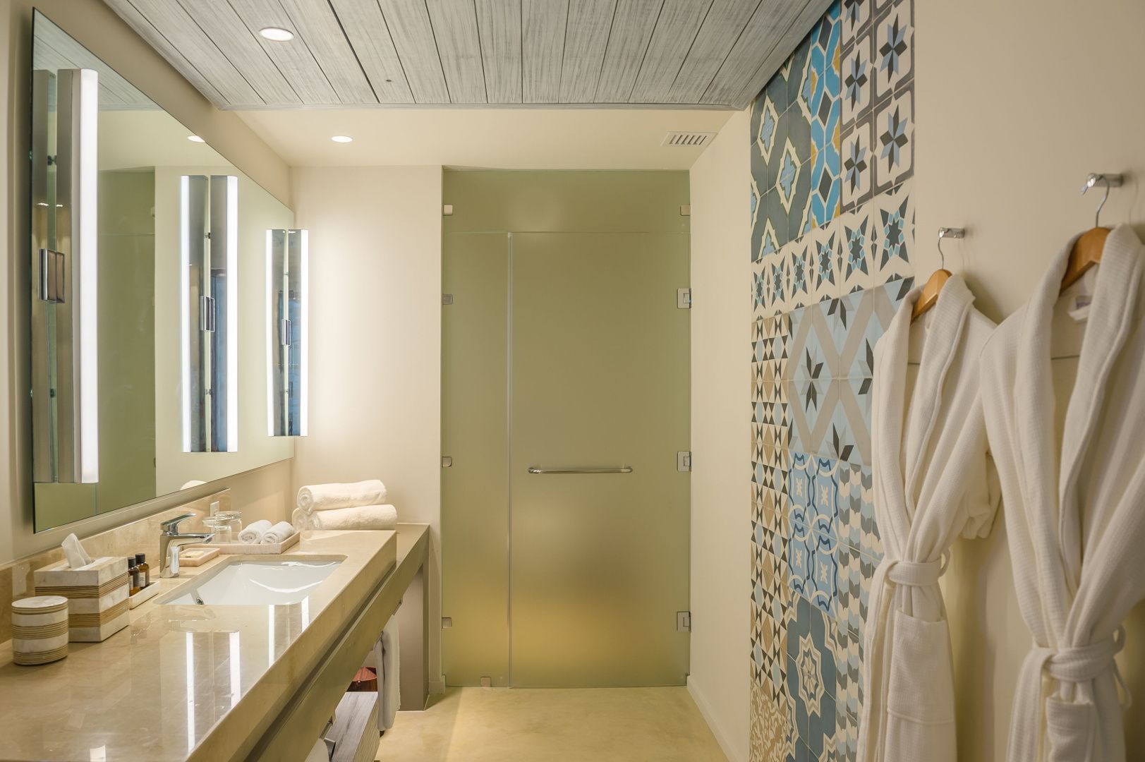Badezimmer mit gemusterten Wandfliesen, Waschtisch und matten Glaselementen.
