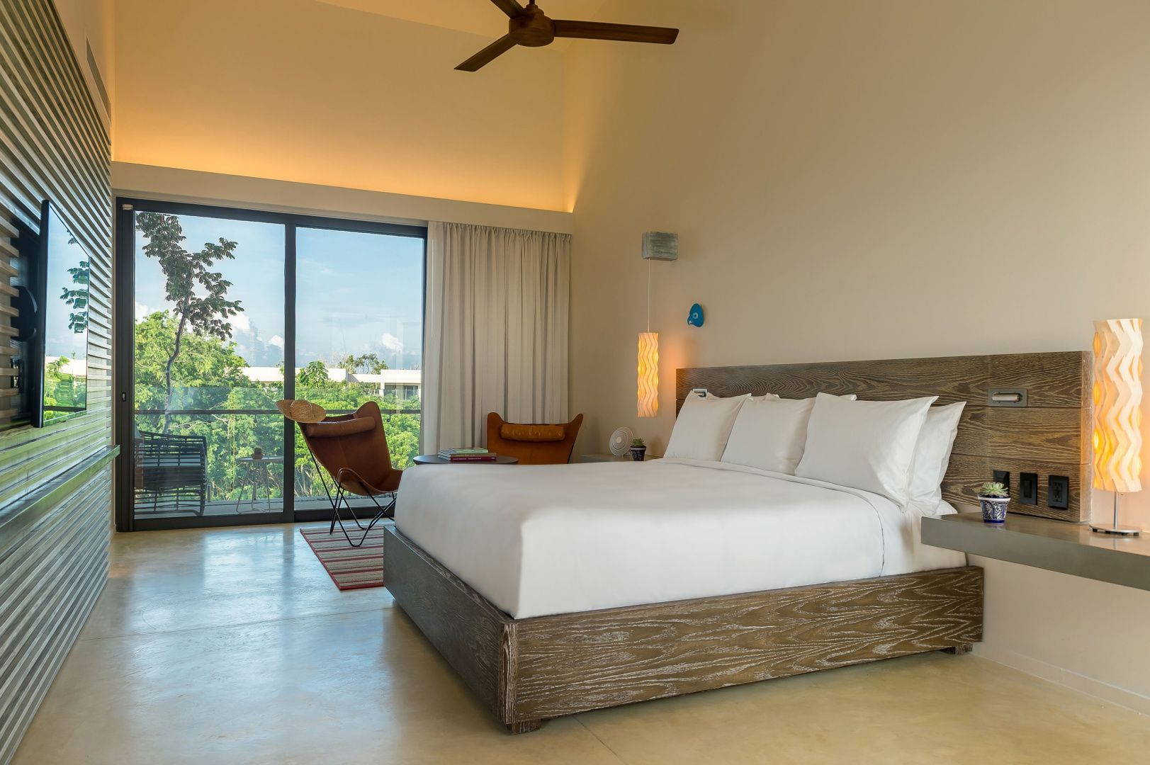 Modernes Hotelzimmer mit grossem Doppelbett, Ledersessel und Balkontür mit Blick ins Grüne.