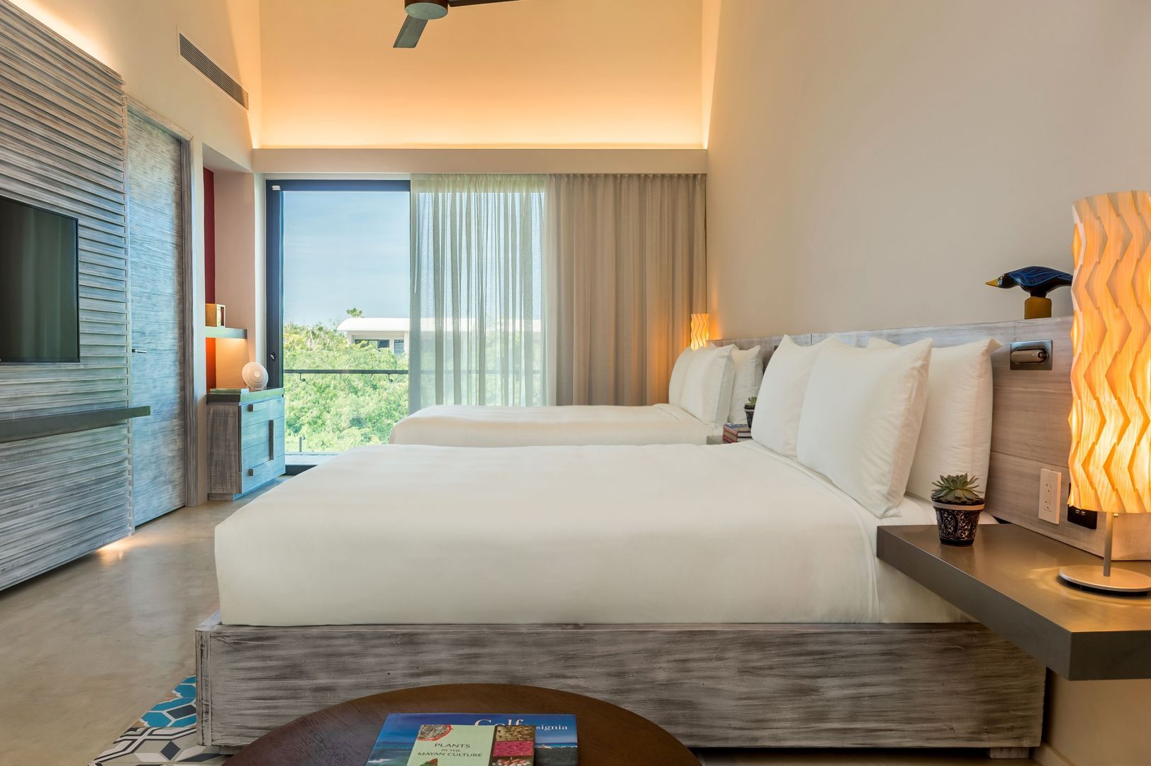 Hotelzimmer mit zwei Betten, indirekter Beleuchtung und grossem Fenster zum Balkon.