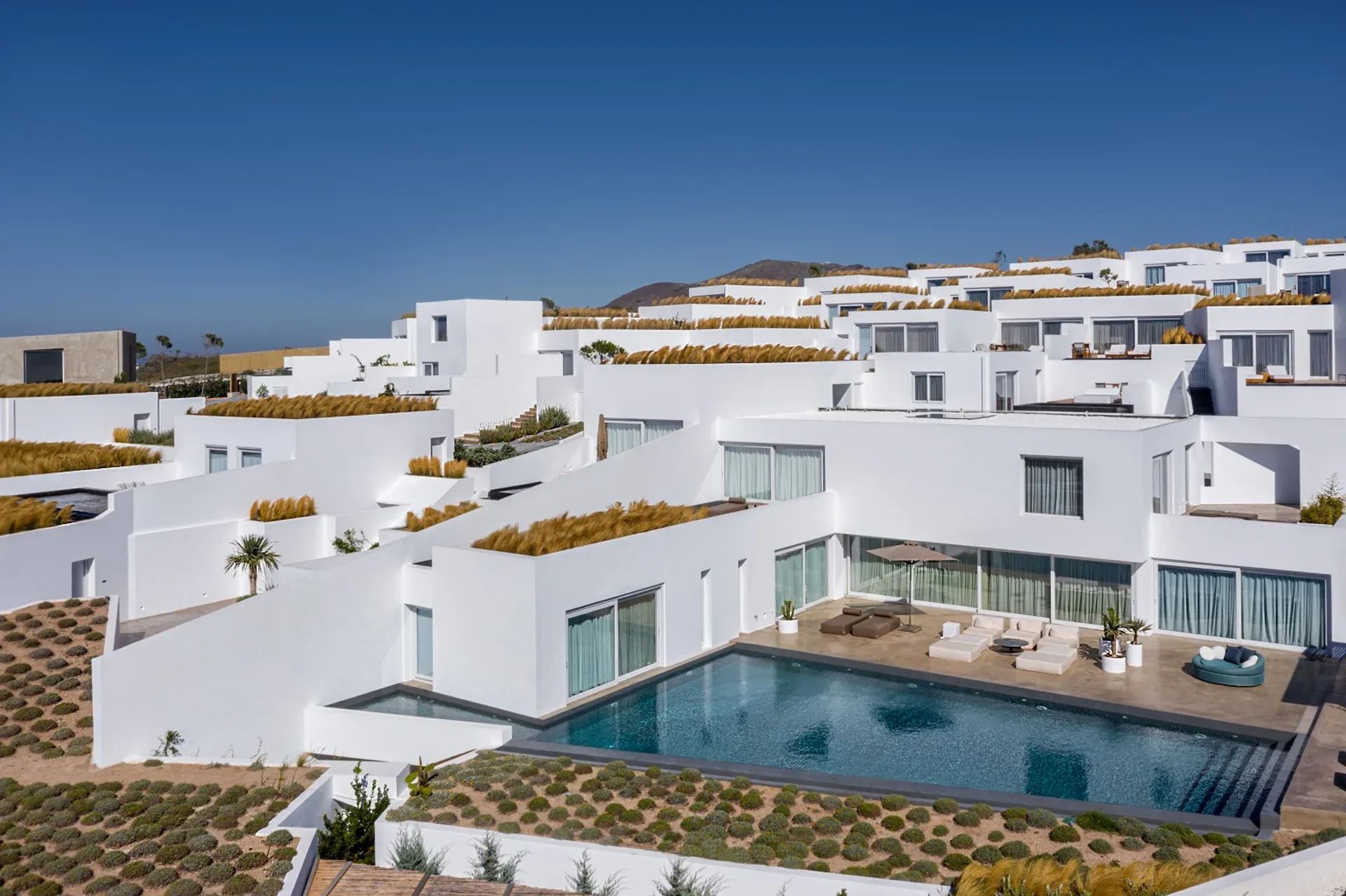 Terrassenförmig angelegtes Luxushotel Andronis Arcadia auf Santorin mit strahlend weißen, kubischen Villen, begrünten Dächern und privaten Pools, unter tiefblauem Himmel in moderner, minimalistisch-mediterraner Architektur.