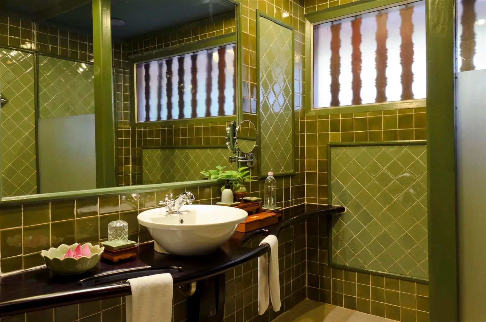 Badezimmer mit grünen Wandfliesen, einem weißen Waschbecken und einem großen Spiegel.