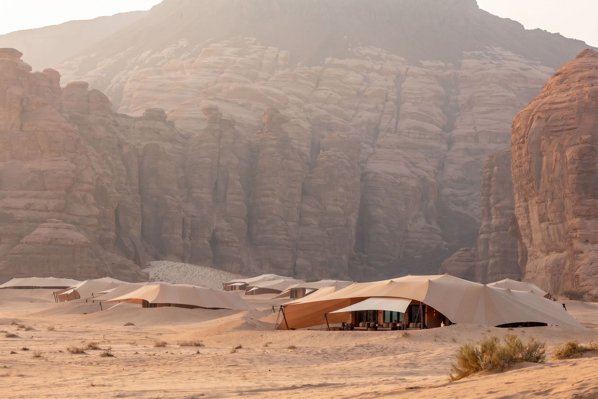 Luxuriöse Wüstenzelte des Banyan Tree AlUla Resorts eingebettet in die sandige, von mächtigen Sandsteinfelsen umgebene Landschaft von AlUla, Saudi-Arabien – in warmem Morgenlicht, das die dramatische Kulisse weich durchleuchtet.