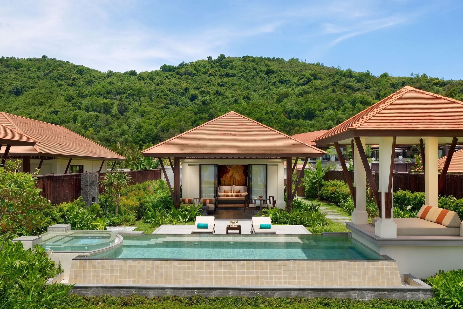 Tropische Villa des Banyan Tree Lang Co Resorts in Vietnam mit privatem Pool, offenen Pavillons und traditionellen Ziegeldächern, eingebettet in üppig grüne Natur und umgeben von bewaldeten Hügeln unter klarem, blauem Himmel.