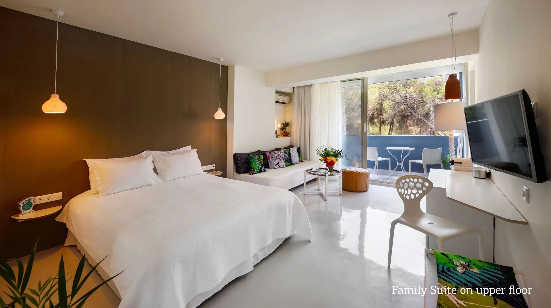 Helles Hotelzimmer mit Doppelbett, weißem Sofa, bunter Kissen-Deko und Balkon im Hintergrund.