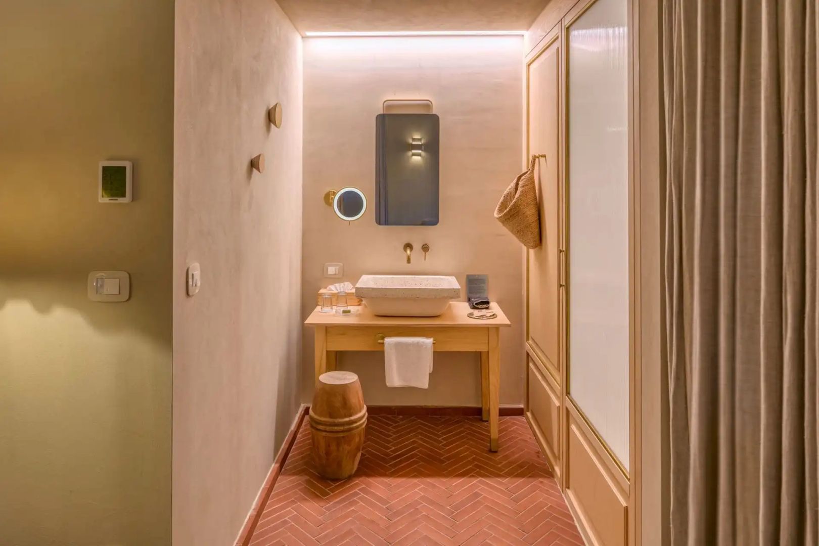 Badezimmer mit Holzwaschtisch, Keramikwaschbecken und beleuchtetem Spiegel.