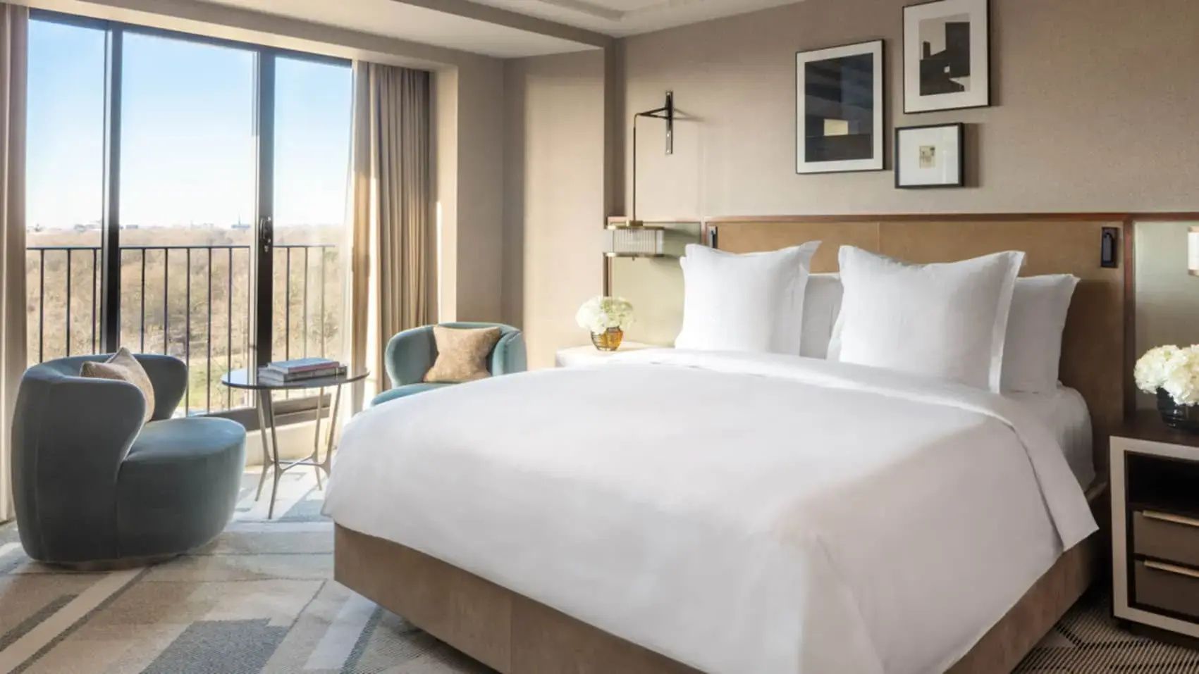 Helles Hotelzimmer mit einem Doppelbett in weißer Bettwäsche, einem hellblauen Sessel und großen Fenstern.