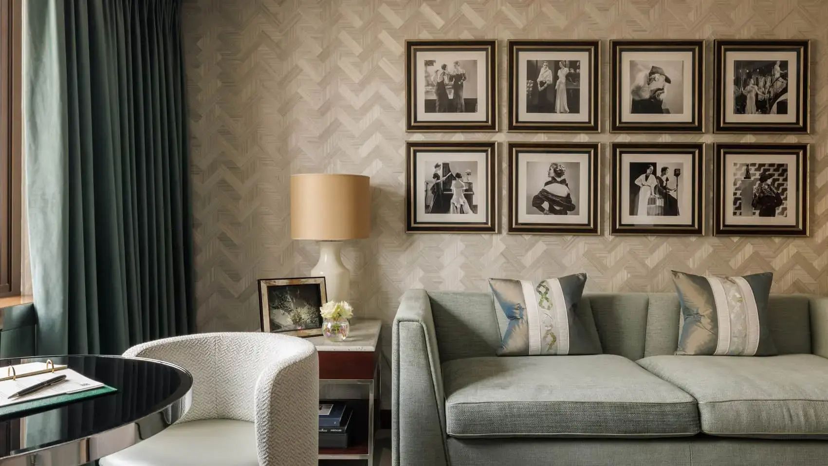 Wohnbereich eines Hotelzimmers mit grünem Sofa, Stehlampe und eingerahmten Fotografien.
