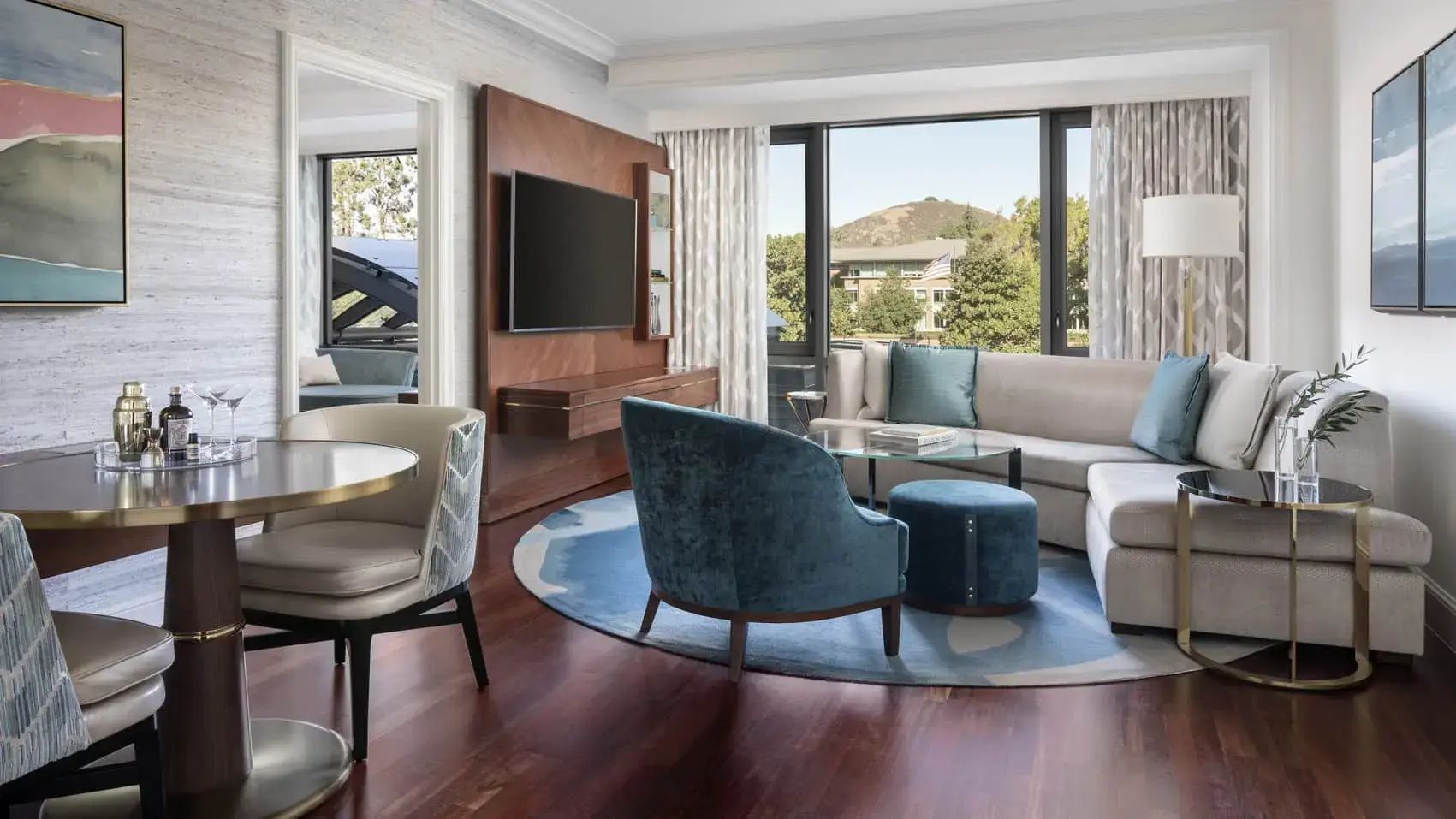 Heller Wohnbereich einer Suite mit hellem Sofa, blauem Sessel, Holzboden und großer Fensterfront.