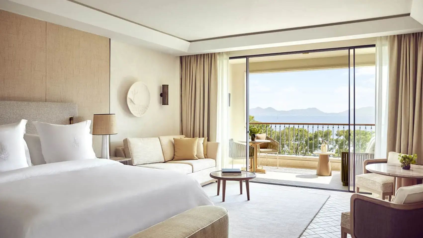 Helles Hotelzimmer mit Sofa, Couchtisch und Balkon mit Blick auf das Meer.