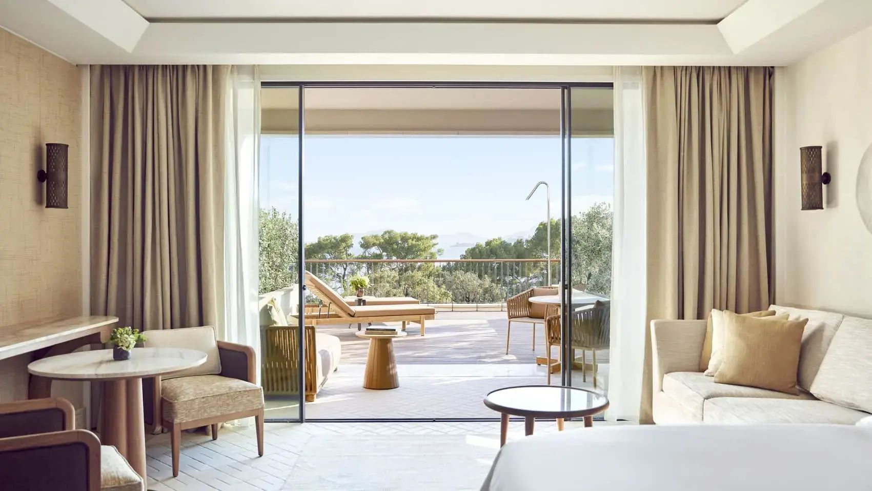 Blick aus einem Hotelzimmer durch große Schiebetüren auf eine Terrasse mit Meeresblick.
