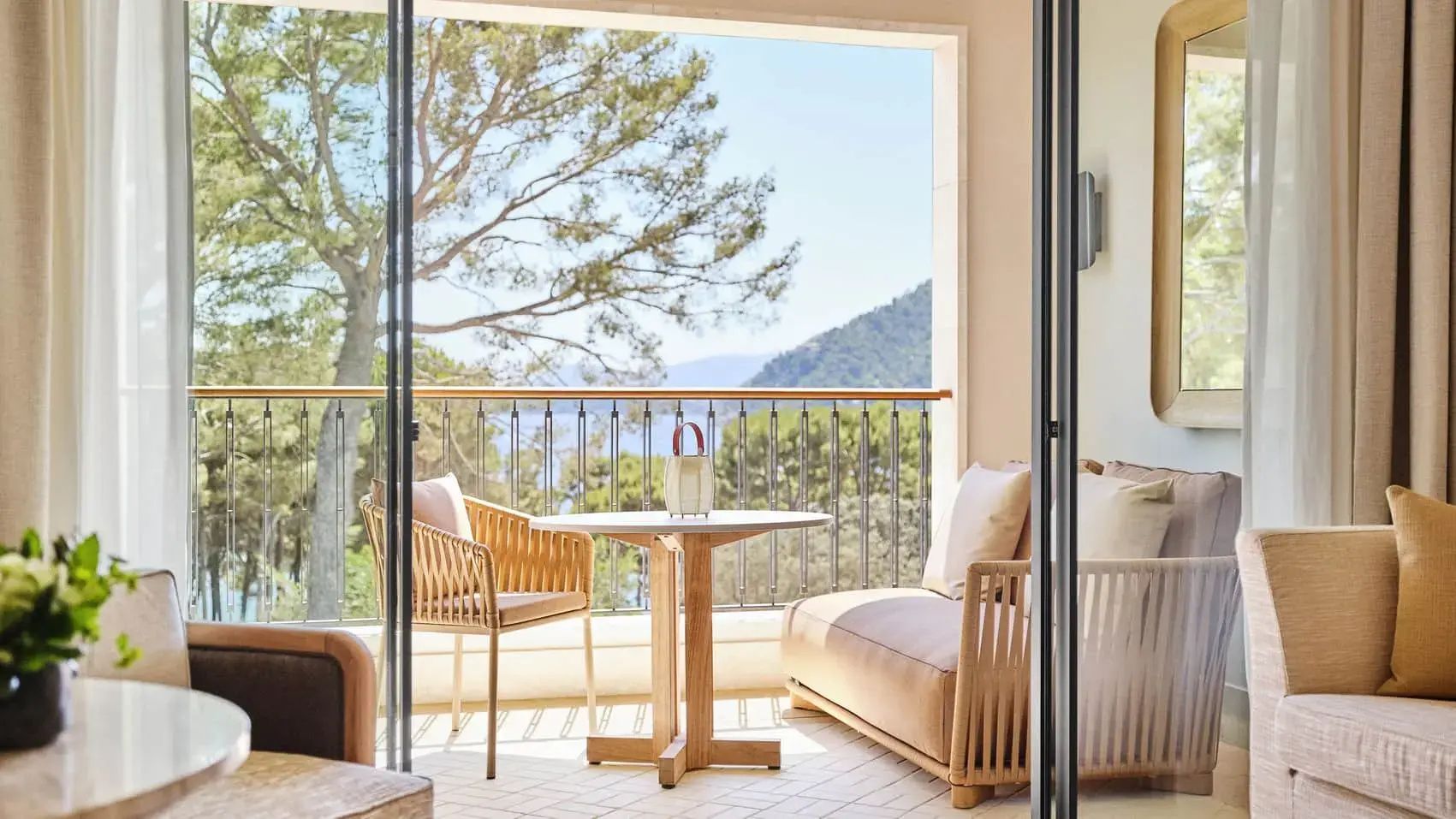 Möblierter Balkon mit Tisch, Stuhl und Bank sowie Ausblick auf Pinienbäume, das Meer und Berge.